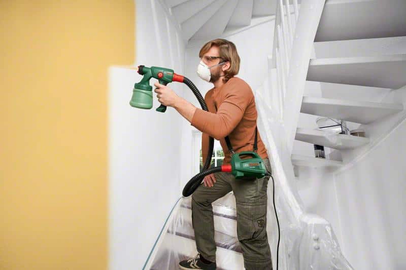 chico pintando pared interior con pistola para pintar